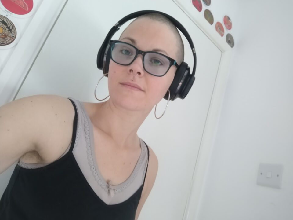 Jenn 2021 - a bald woman wearing headphones and glasses