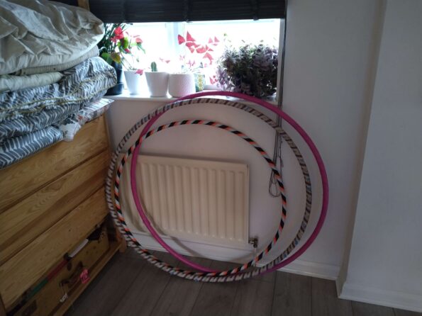 Three colourful hulahoops lean against a wall in front of a radiator and window