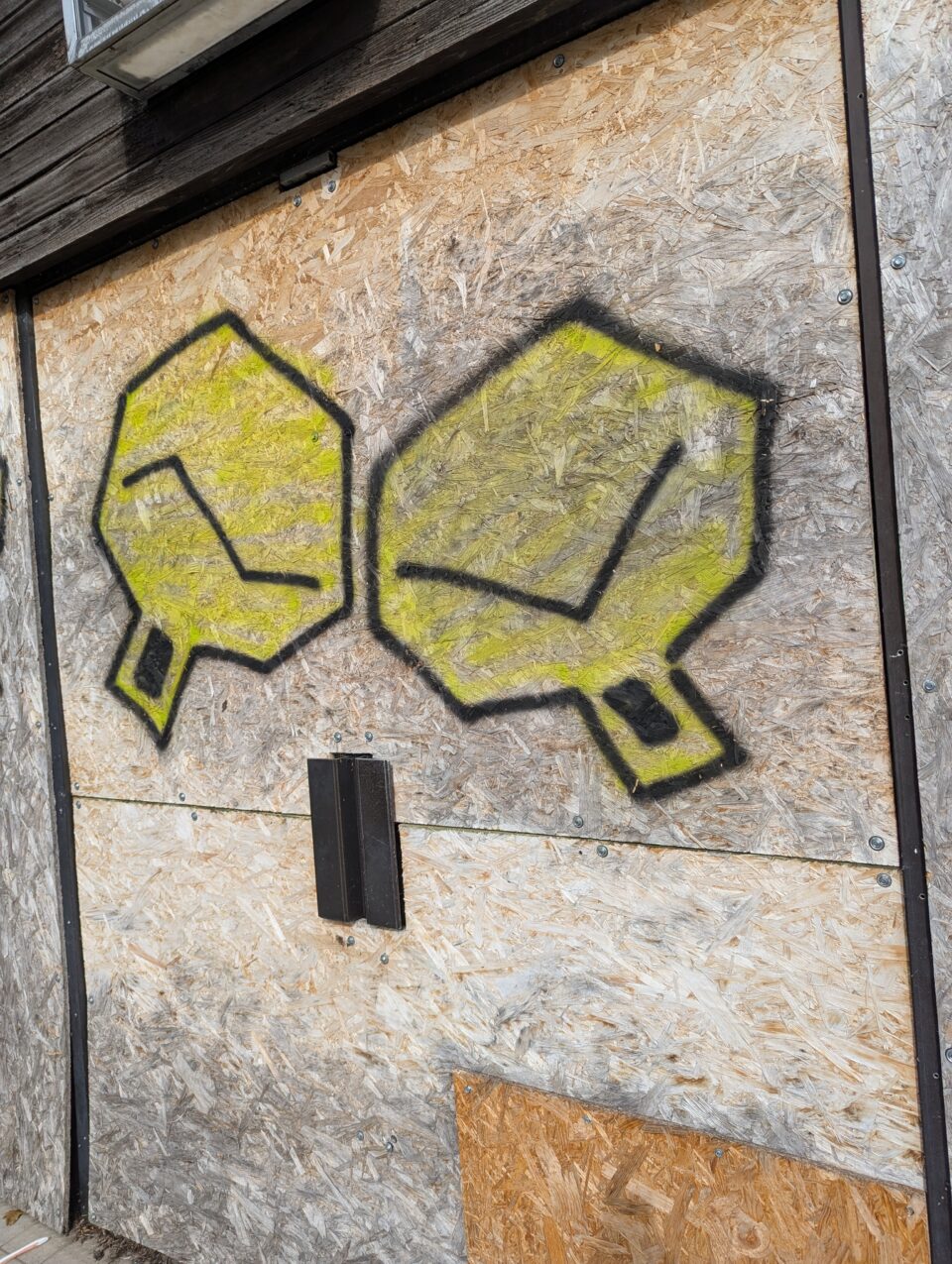 Two yellow and black angular graffiti symbols painted across weathered wooden boards.