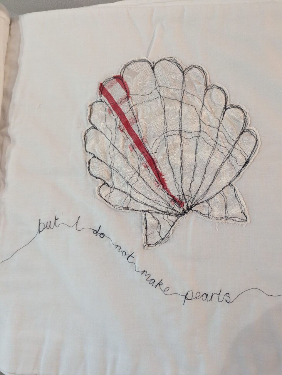 Textile shell form outlined in black thread with a red strip, above the stitched words “but I do not make pearls”.